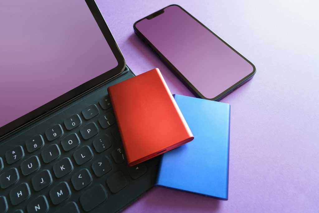 Un ordinateur portable, un téléphone et une batterie externe sur une surface violette.