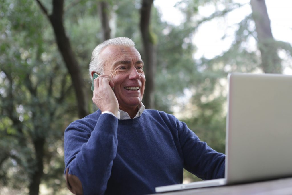 Un homme assis à une table, utilisant un ordinateur portable tout en parlant au téléphone.